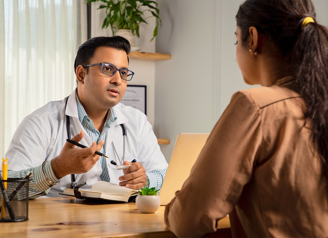 Employee Benefits - Male Physician Wearing White Apron and Stethoscope With File of Medical Report Is Giving Mental Support to a Young Female Patient